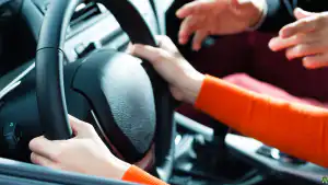 Driving instructor teaching a learner to control the steering wheel