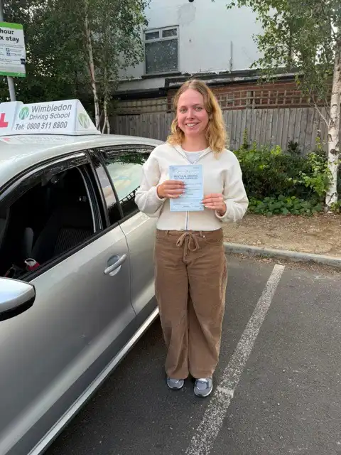 Alice holding her driving test pass certificate beside a Wimbledon Driving School car