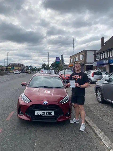 Johnny holding his driving test pass certificate beside a Wimbledon Driving School car